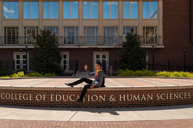 Leo wearing a graduation stole outside the College of Education and Human Sciences.