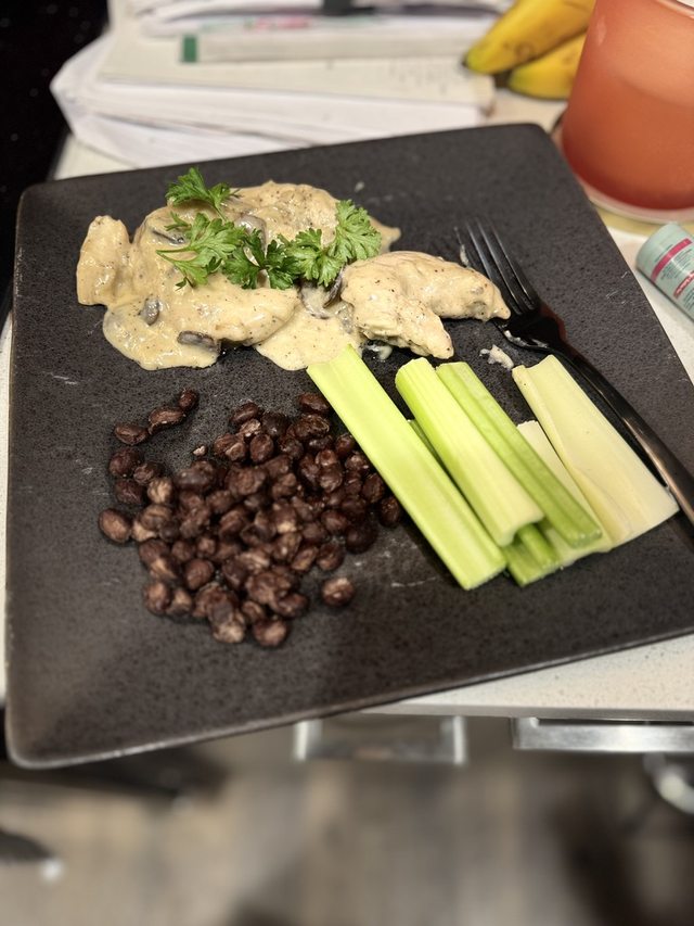 A home-cooked meal with chicken in a creamy sauce, black beans, and celery on a dark plate.