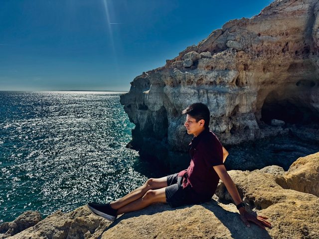 Leo sitting on sandstone cliffs beside sparkling ocean water.