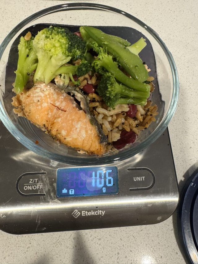 Salmon, rice, beans, and green vegetables in a bowl on a kitchen scale.