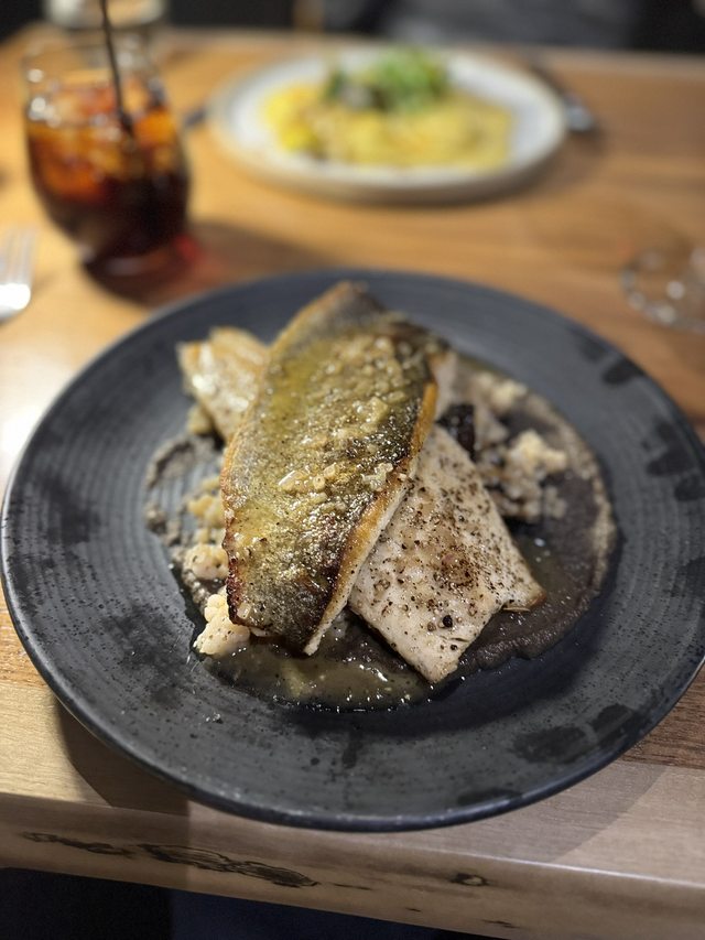 A restaurant fish dish served on a dark plate at a wooden table.