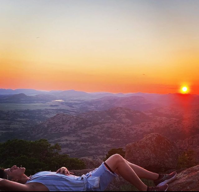 Leo resting on a rocky overlook at sunset, with rolling hills in the distance.